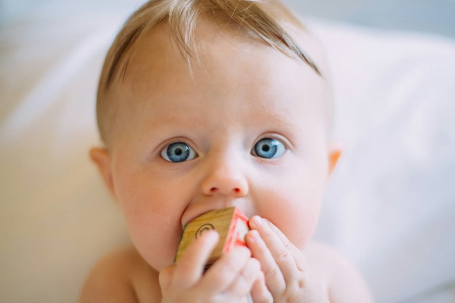 a baby with blue eyes biting a block